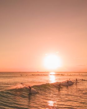 在夏季的海滩上，冲浪者在充满活力的日落天空下冲浪，海面反射出温暖的橙色色调
