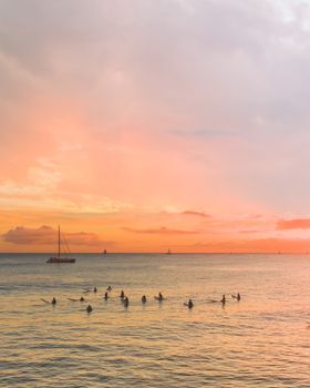 夕阳西下，海面宁静，冲浪者划着船，帆船的轮廓映衬在充满活力的天空下