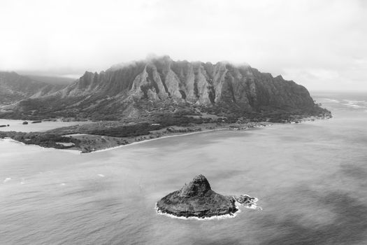 Black and white aerial shot of a rocky island and lush mountain range with ocean views.