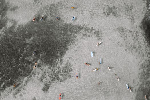 航拍照片捕捉到了夏季平静海面上，冲浪者站在彩色冲浪板上的画面