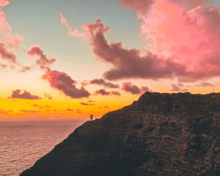 崎岖的海岸线上，灯塔矗立，天空充满活力，日落景象令人惊叹