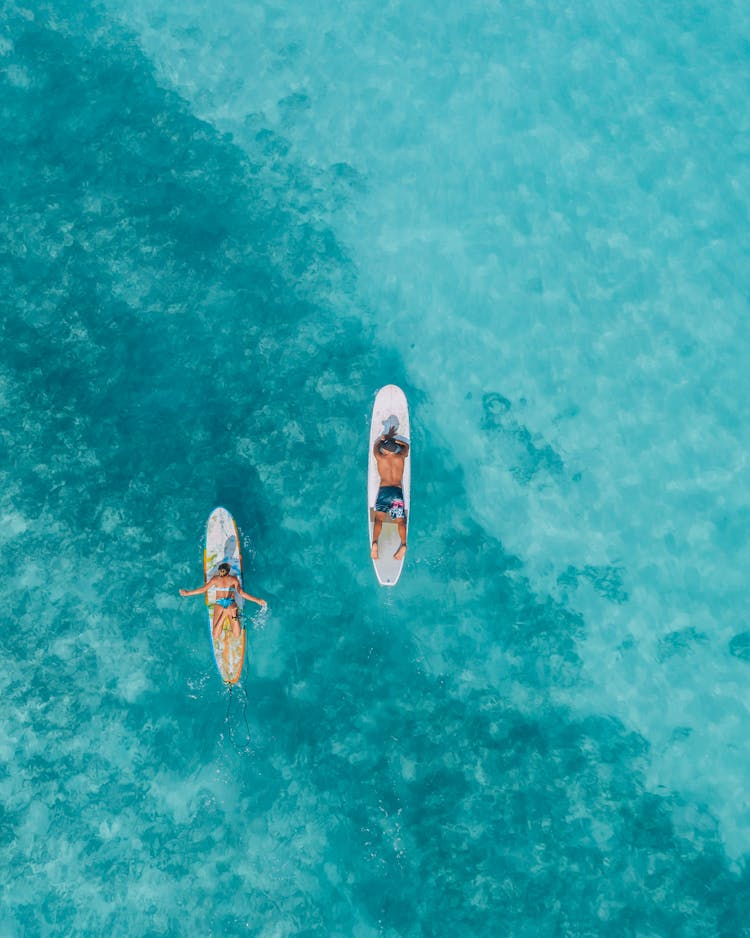 Couple Lying On Surfboards Swimming Into Ocean