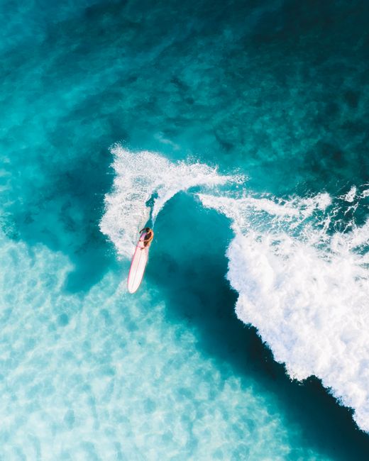 Drone shot of a surfer carving a wave in bright turquoise water, showcasing summer recreation.
