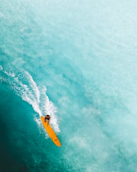 动态航拍照片捕捉到了一名冲浪者驾着黄色冲浪板穿过碧绿海浪的瞬间，展现了海洋冒险的精髓