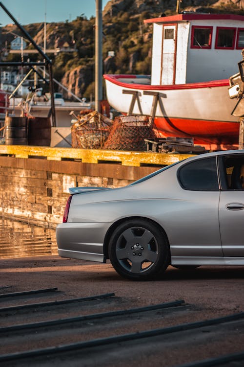 Posterior part of gray tuned sports car parked on coast of wavy reservoir in seaport near mountain valley