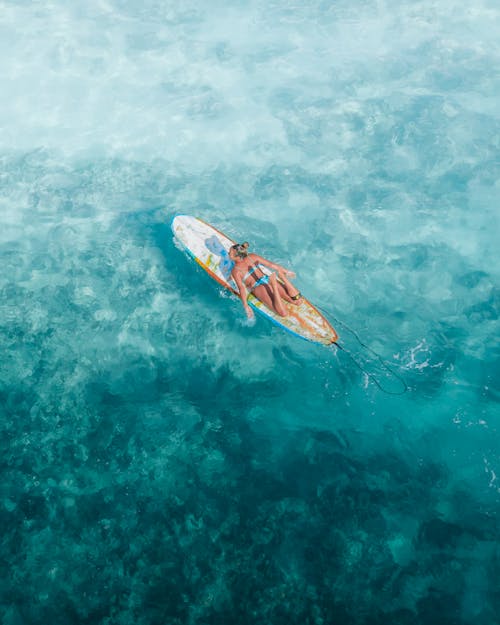 Free Woman Lying on a Surfboard on a Blue Sea Stock Photo