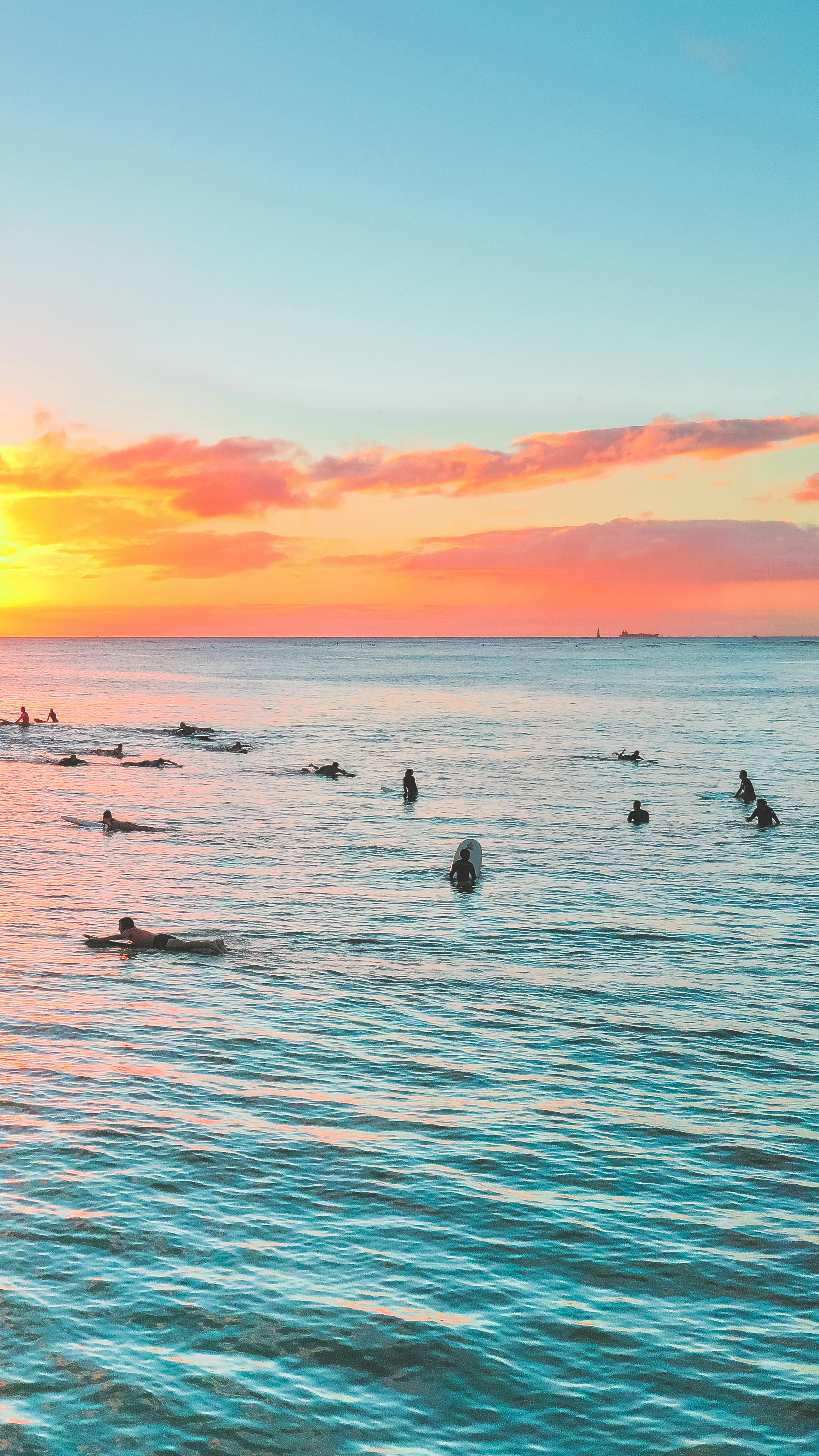 冲浪者在充满活力的日落中在平静的海水中捕捉海浪，天空色彩缤纷