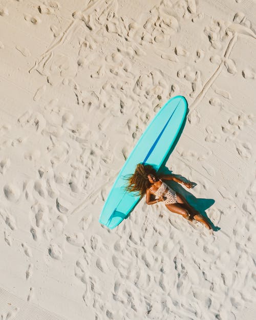 Top View of Woman With Hair Toss Lying on a Turquoise Surfboard on Sand