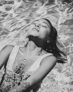 这是一张黑白照片，照片中一名女子正在喝水，她纹身明显，表情安详