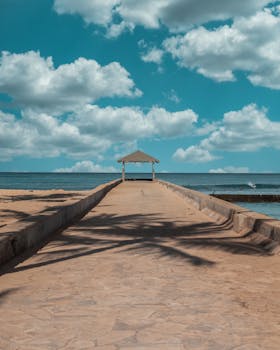 Peaceful walkway leading to a gazebo by the sea with a clear blue sky and ocean.