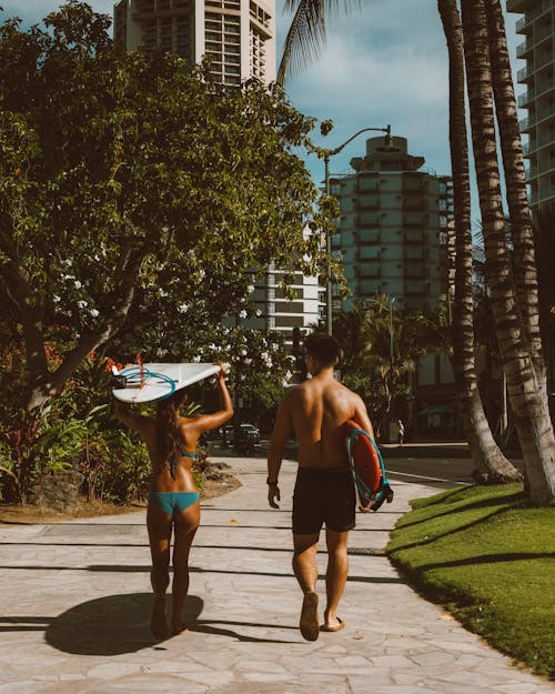 A Man and Woman in Swimsuits Carrying Surfboards
