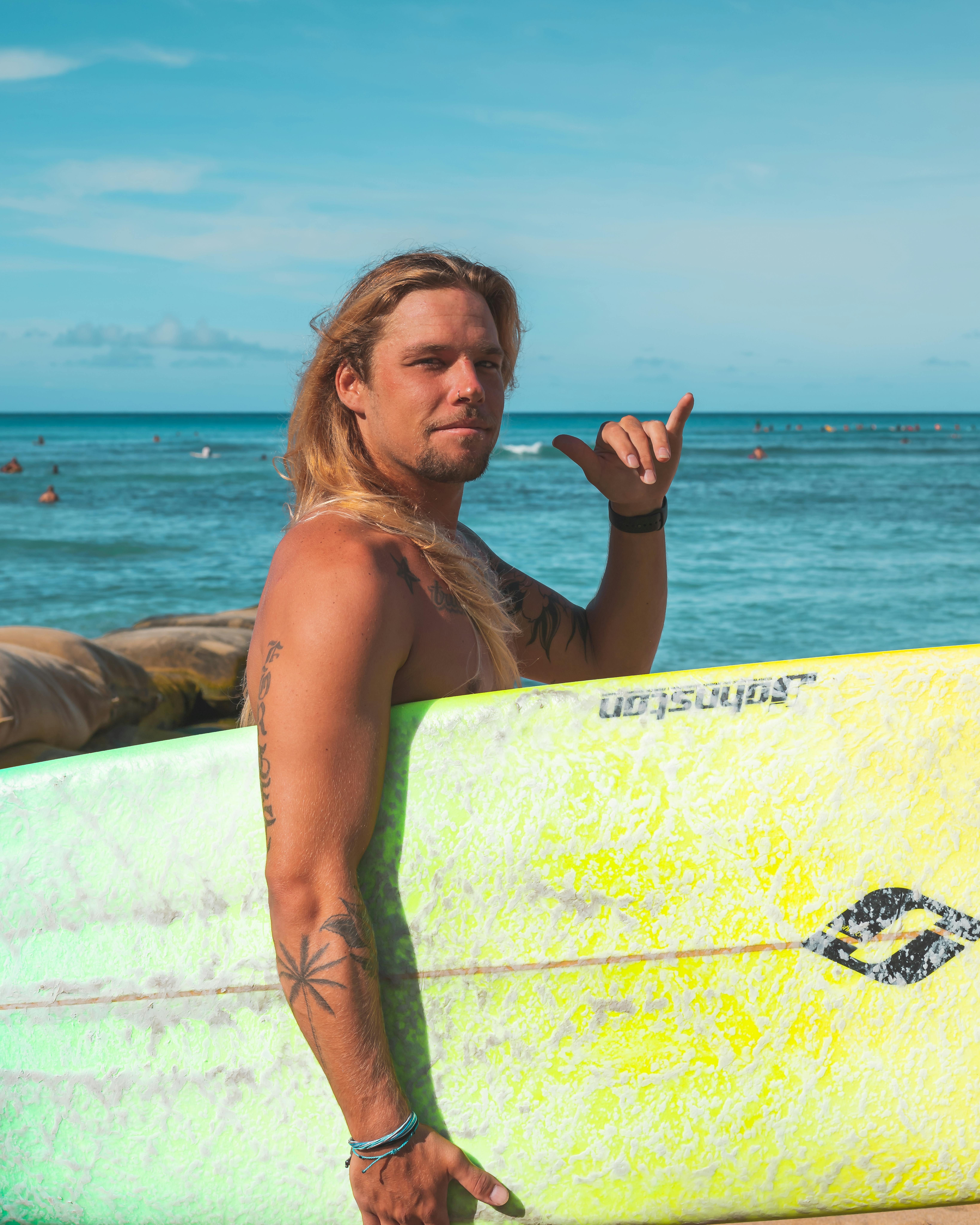 纹身的冲浪者显示沙卡标志，而持有冲浪板在海滩上，代表一种轻松的生活方式