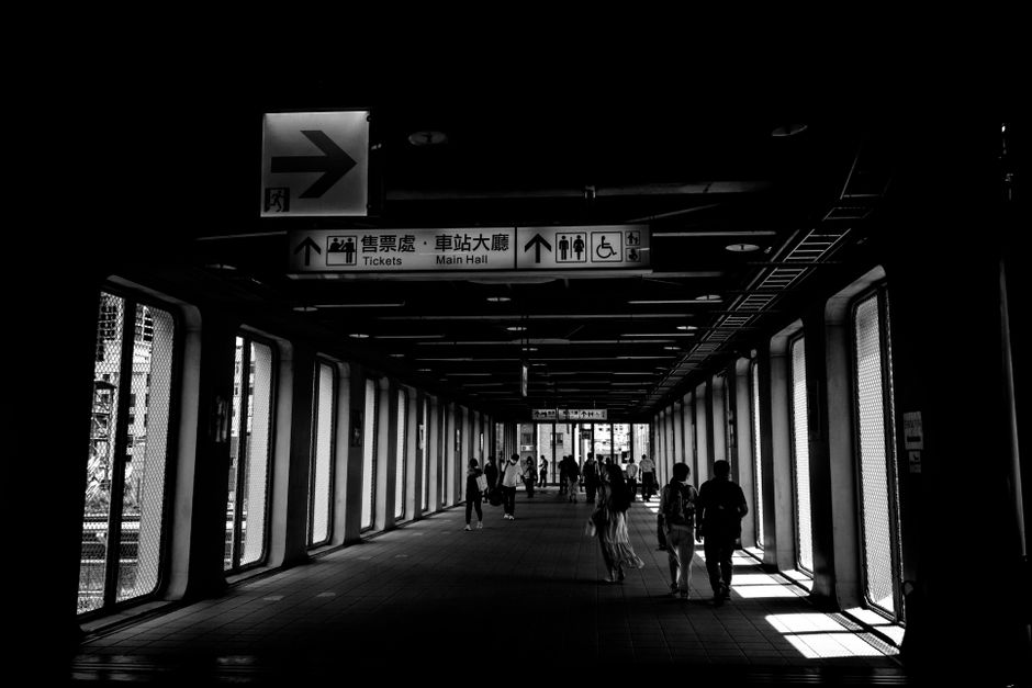 A black and white image showing people walking inside a modern train station in Taipei, Taiwan.