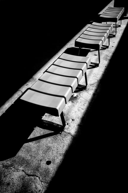 A row of empty chairs casting long shadows on the ground in stark black and white.