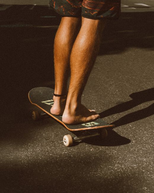 Close-up of a person's legs skateboarding barefoot on a sunny pavement, showcasing balance and lifestyle.