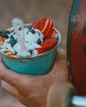 Close-up of a vibrant acai bowl topped with strawberries and blueberries, held in hand.