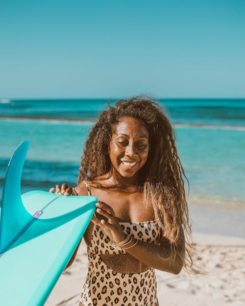Smiling Woman Holding a Blue Surfboard on the Beach