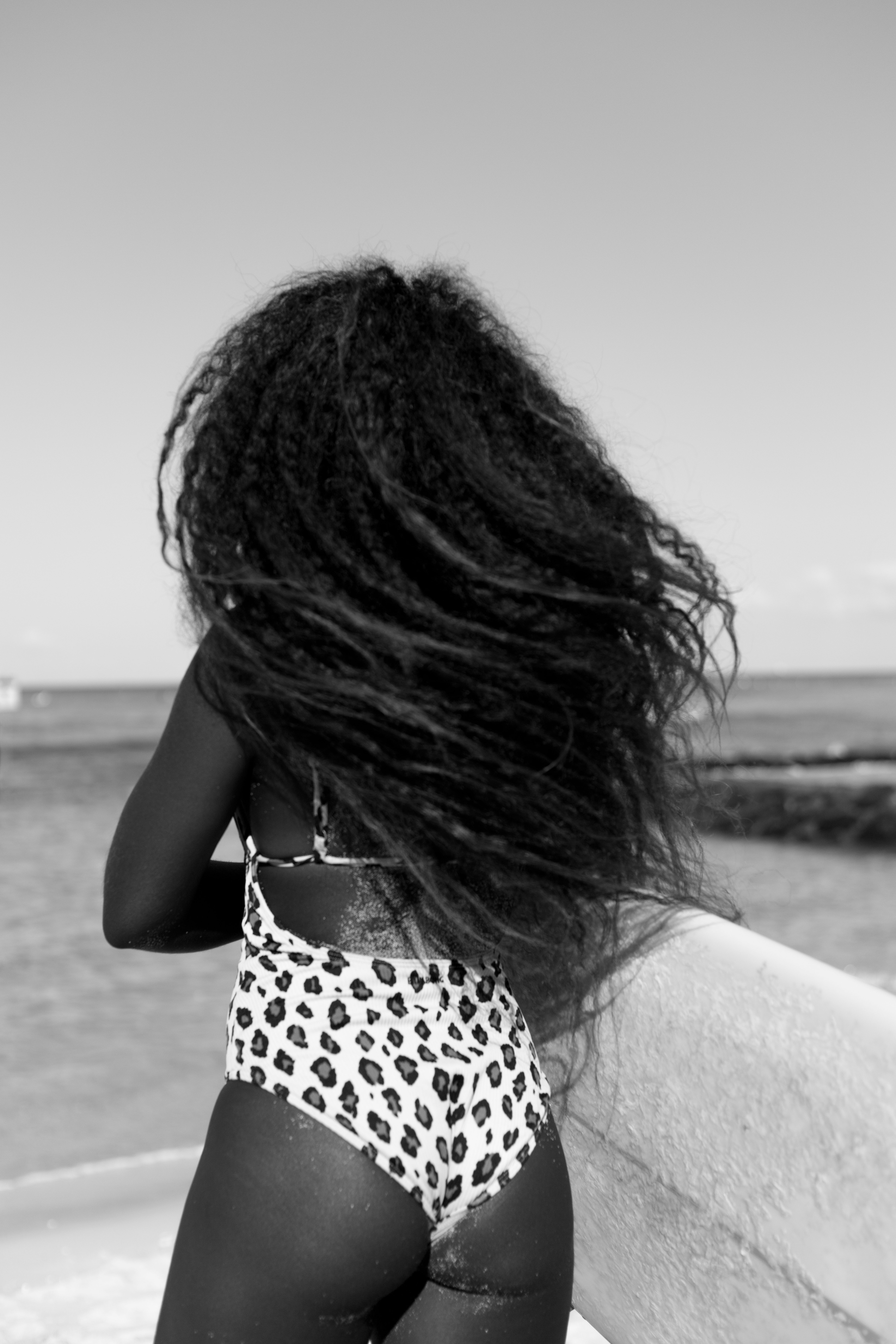 Woman with long hair in a swimsuit looking at the ocean, monochrome image.