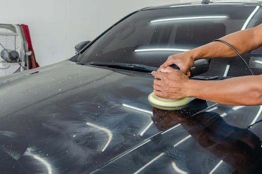 Close-up of a mechanic polishing a car's surface in an indoor auto workshop.