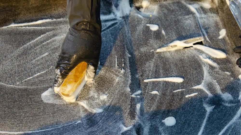 A detailed view of cleaning in progress, focusing on a gloved hand using a brush with detergent on a surface.