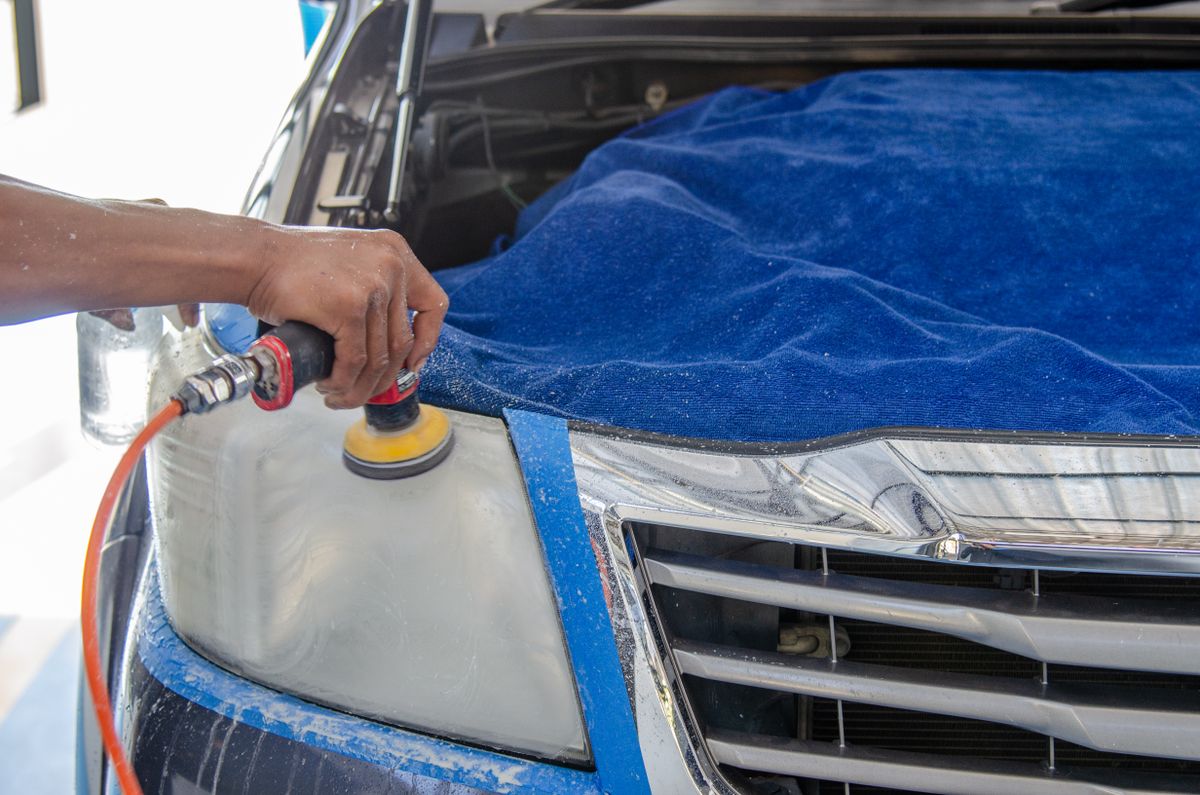 A technician using a dual-action polisher to restore a taped-off car headlight