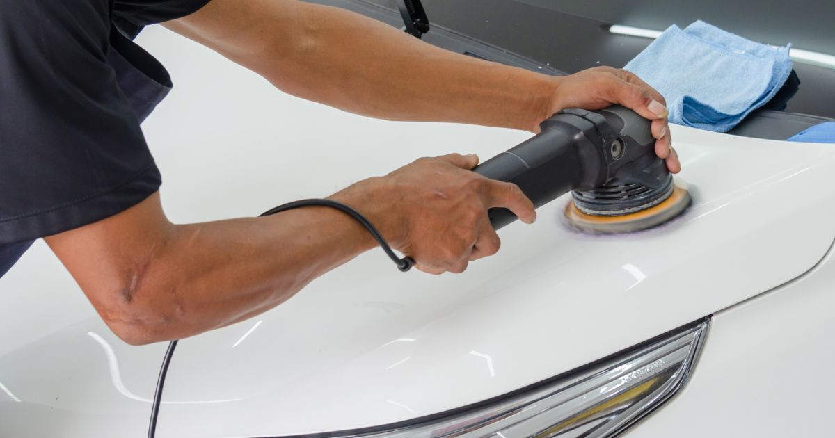 A man running a black dual action polisher over the bonnet of a white car in a bright workshop