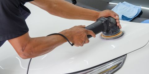 A man running a black dual action polisher over the hood of a white car in a bright workshop