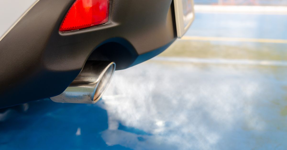 A close view of a car's exhaust pipe emitting smoke on a sunny day, highlighting pollution.