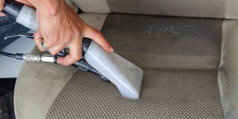 A hand vacuuming a fabric car seat