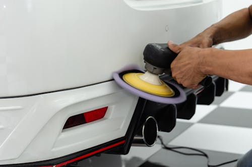 Person Polishing the Back of the White Car After Muffler Installation