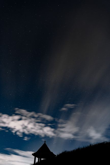 Silhouette of a house under a starry night sky with flowing clouds.