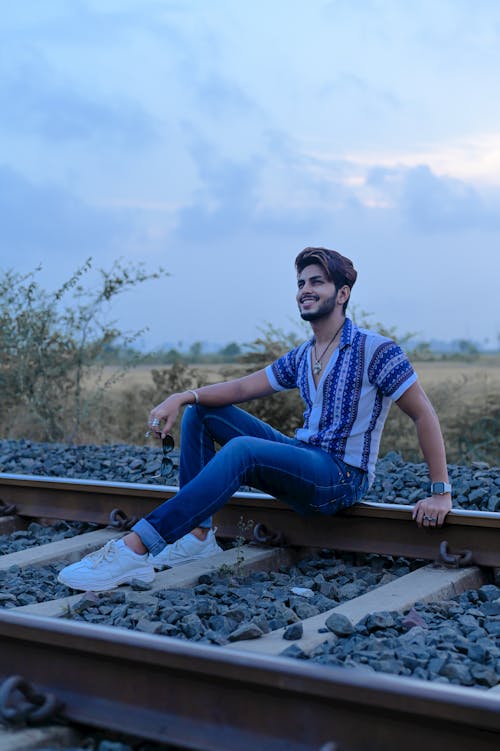 Cheerful man in stylish clothes sitting on railway