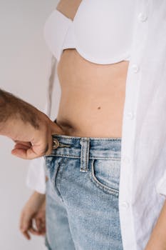 亲密特写中，一只手握着未系扣的牛仔裤腰带，上腹部清晰可见