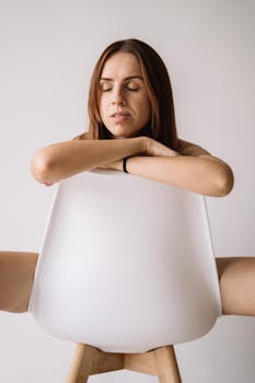 一位成年女性闭目静坐，在简约环境中，放松地坐在现代白色椅子上