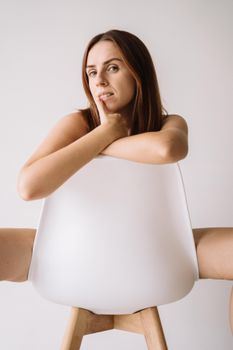 室内中性背景前，一位女性坐在现代椅子上，创意与时尚兼具的肖像