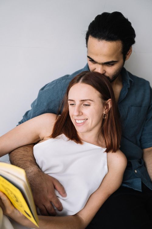 Free A joyful couple sitting close, enjoying a book together indoors. Stock Photo