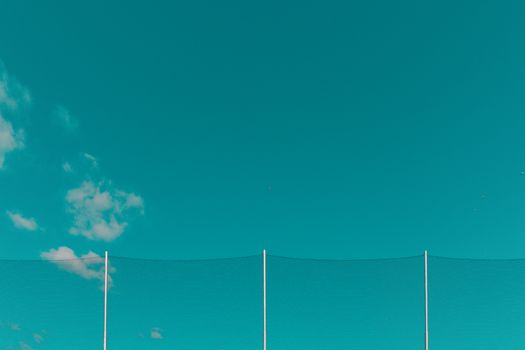 Minimalist outdoor scene with a teal sky, gentle clouds, and netting. Ideal for backgrounds.
