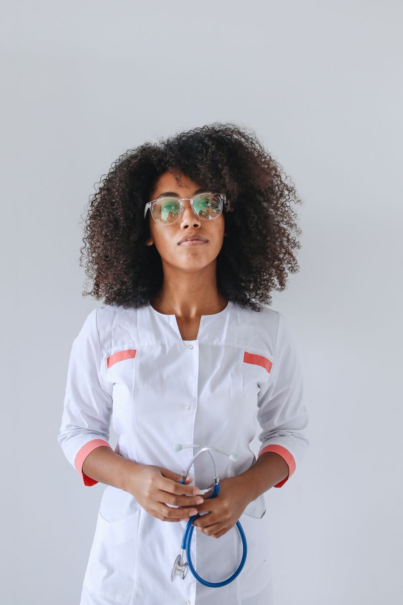 A Black female physician in a white coat holds a stethoscope, representing the neurologists who diagnose and treat multiple sclerosis in Black patients.