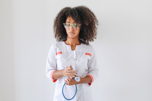 Free Female doctor with curly hair and eyeglasses holding a stethoscope, looking confidently at the camera. Stock Photo