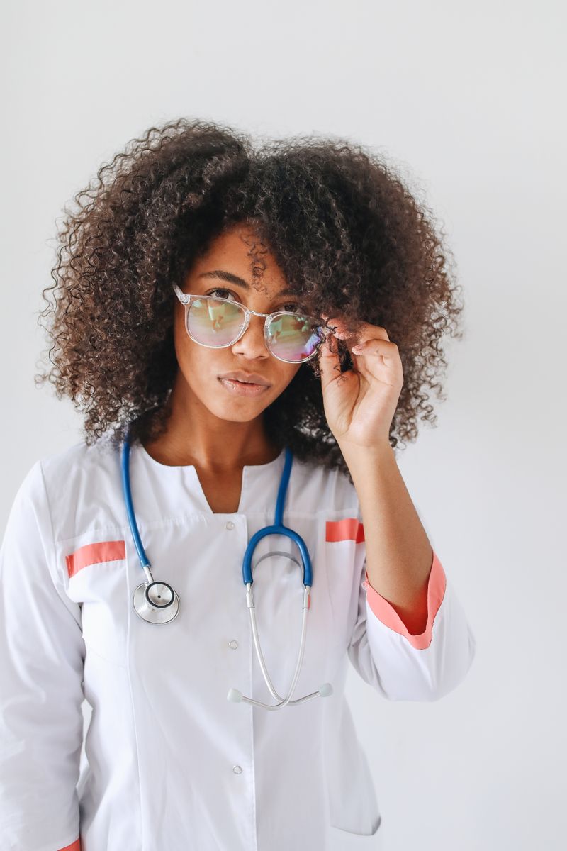 Portrait of a female doctor with afro hair wearing glasses and a stethoscope.