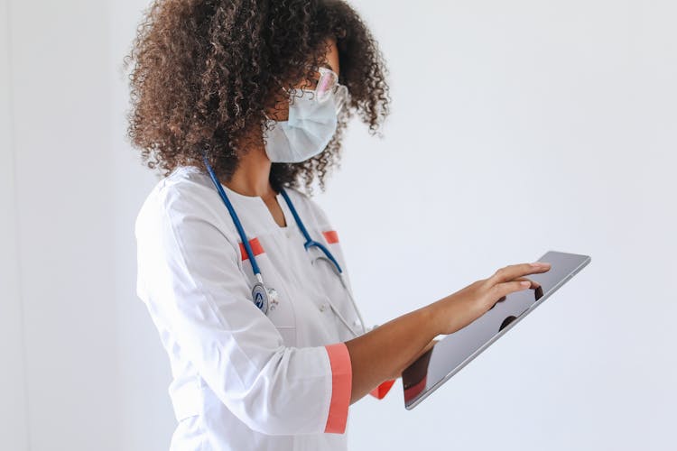 A Doctor Wearing A Face Mask Using A Tablet