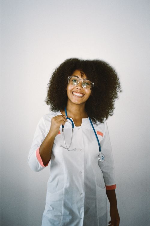 Free Smiling female doctor with curly hair wearing eyeglasses and stethoscope, embodying healthcare professionalism. Stock Photo