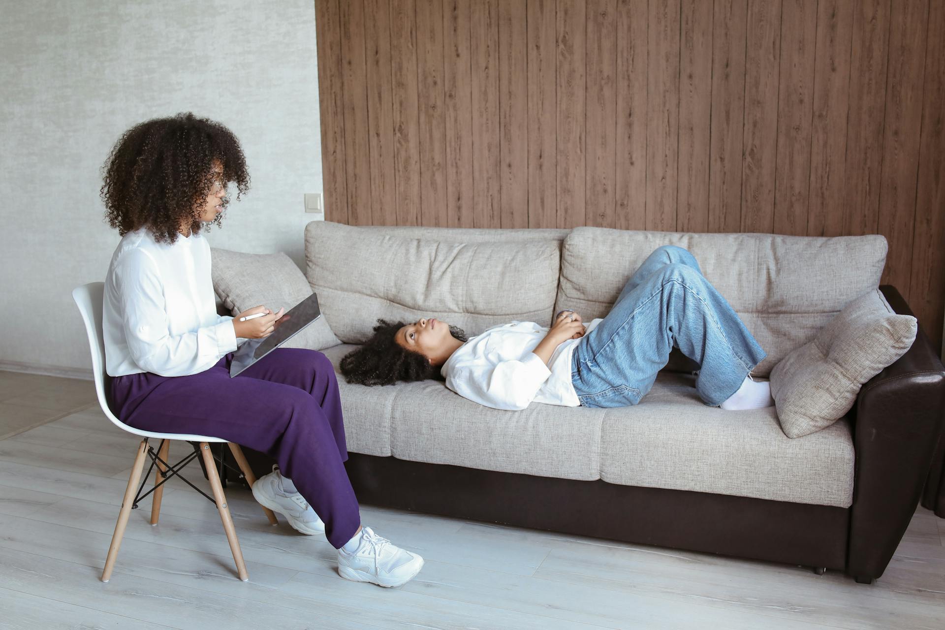 Therapist with a tablet consulting a client lying on a sofa during a counseling session.