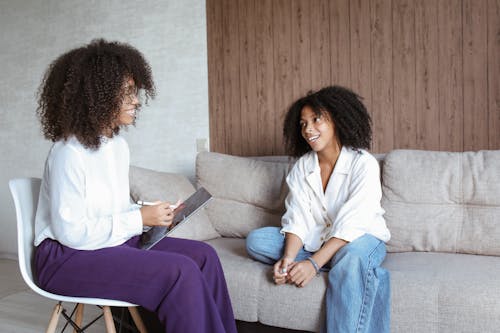 Woman in White Long Sleeve Shirt and Blue Denim Jeans Sitting on Gray Couch