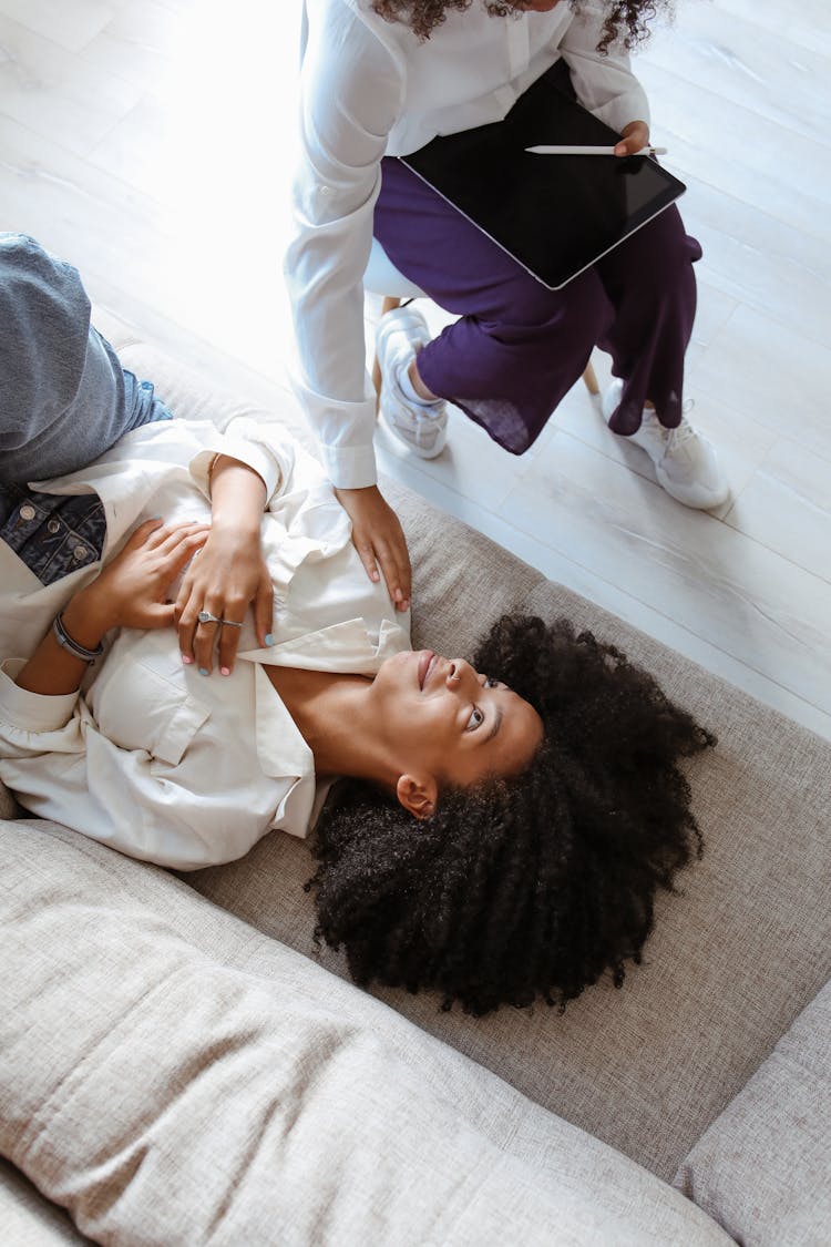 A Person Sitting On The Chair Touching A Woman's Shoulder Lying On The Couch