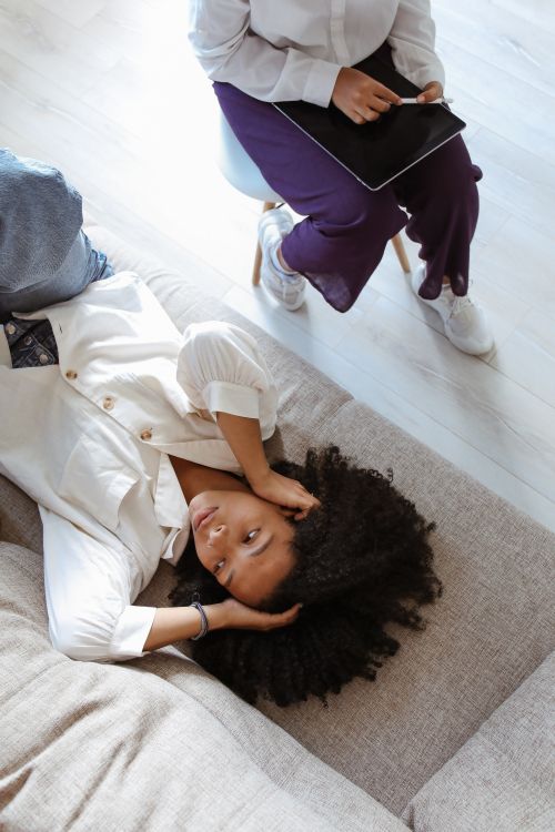 Free African American woman with afro hair lying on a couch, hands on head, in a calming indoor setting. Stock Photo