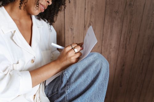 Free Close-up of a woman writing on paper, sitting peacefully indoors with natural lighting. Stock Photo