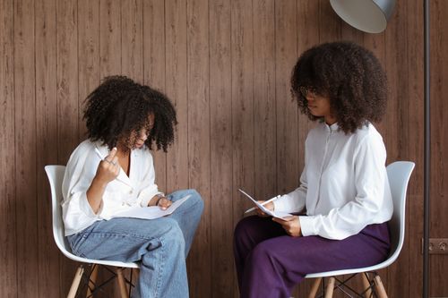 Free Two women engaged in a conversation while seated indoors, holding papers. Stock Photo