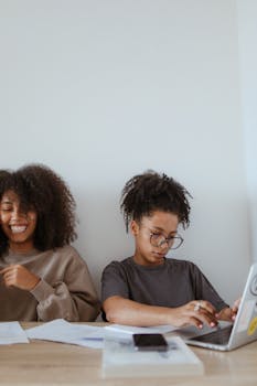 Young women working and smiling at home with documents and a laptop, embodying a relaxed work environment.