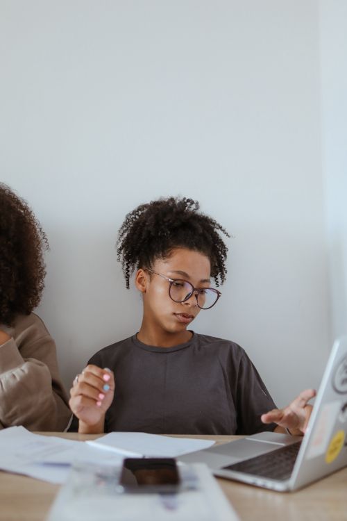 Free Focused young woman with glasses working on a laptop from home. Perfect for technology and remote work themes. Stock Photo